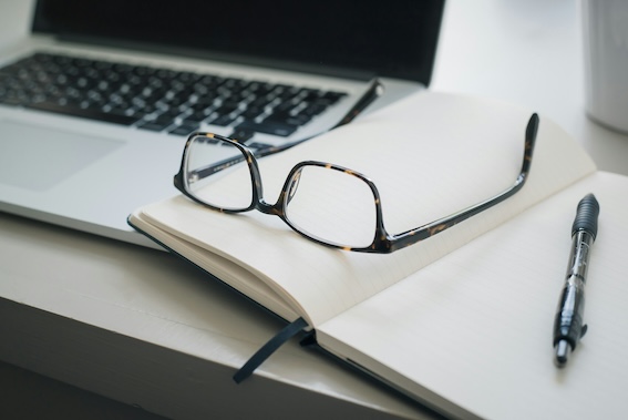 Aufgeklappter Laptop mit Notizbuch, Stift und Brille